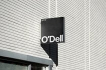 Black square storefront sign with O'Dell branding mounted on ribbed metal wall
