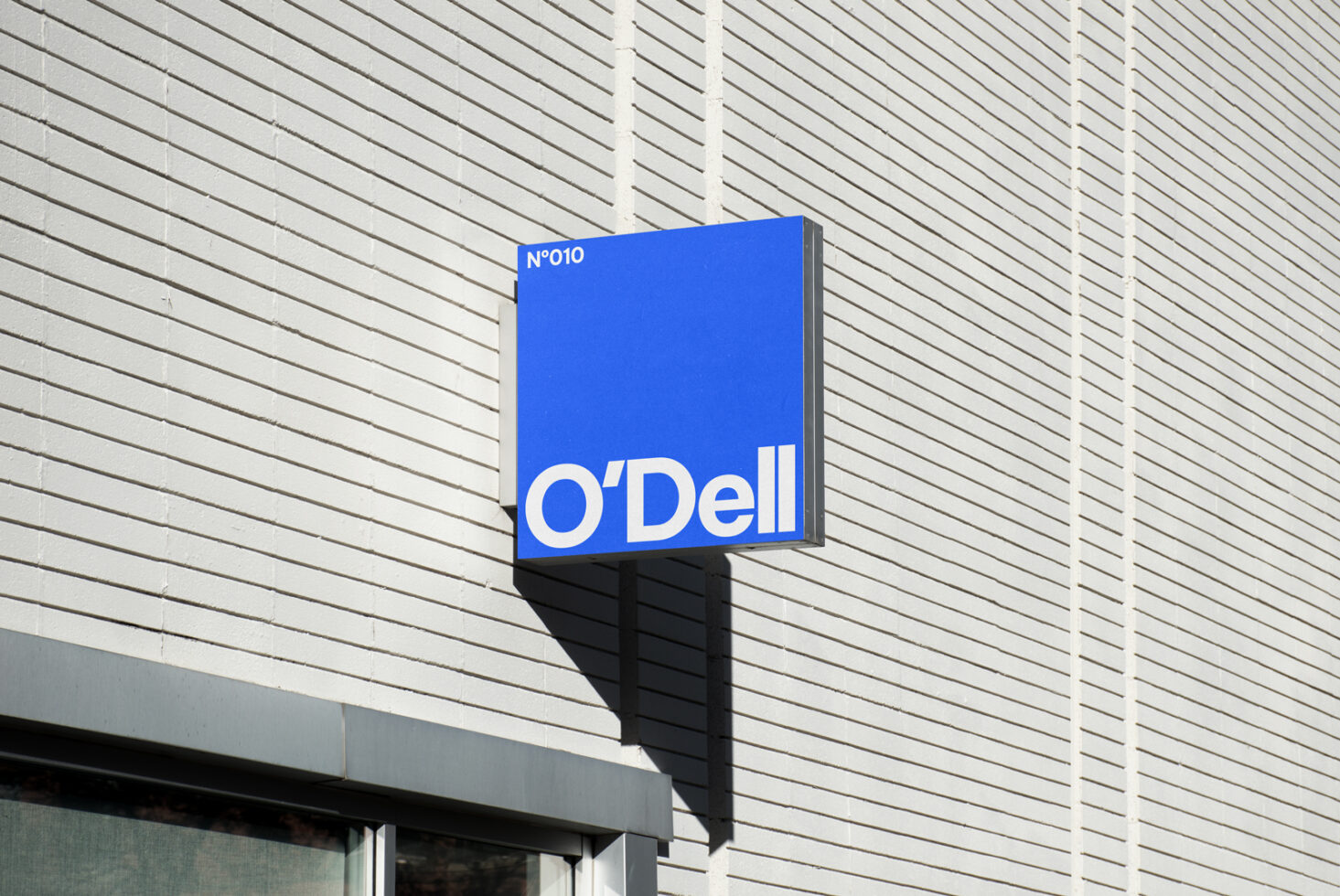 Blue storefront sign mockup with minimal white text on a brick wall. Ideal for branding design templates and graphic designers seeking signage displays.