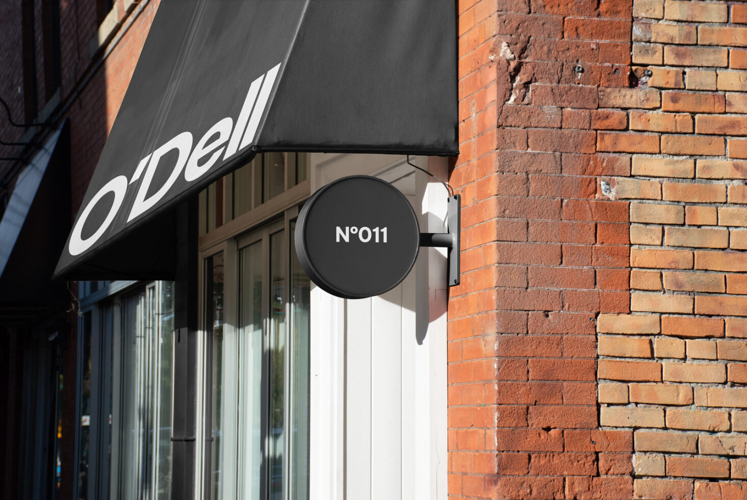 Storefront signage mockup on brick building with black awning and circular sign. Perfect for showcasing logos, branding, and graphic design projects.