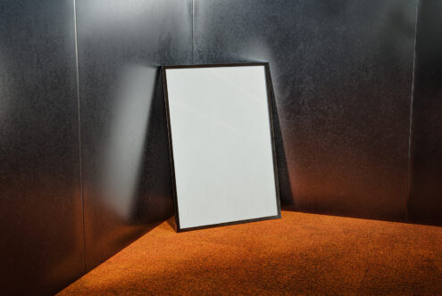 Minimalist frame mockup leaning against a metallic wall with an orange textured floor background perfect for presentations and design showcases.