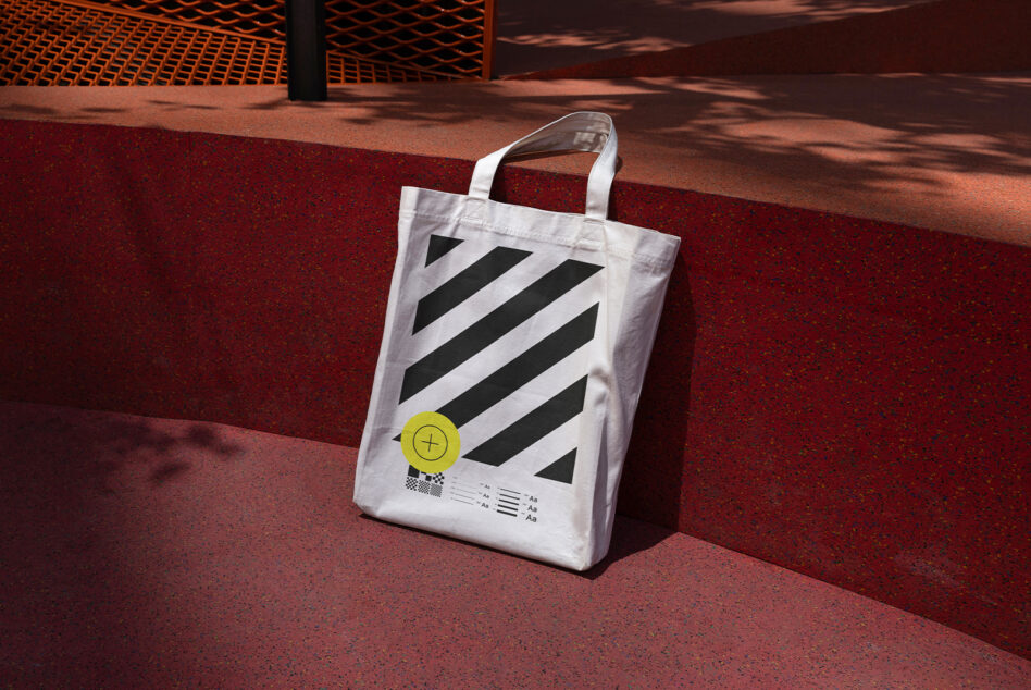 White canvas tote with diagonal stripes, yellow circle, tested mockup on red ground