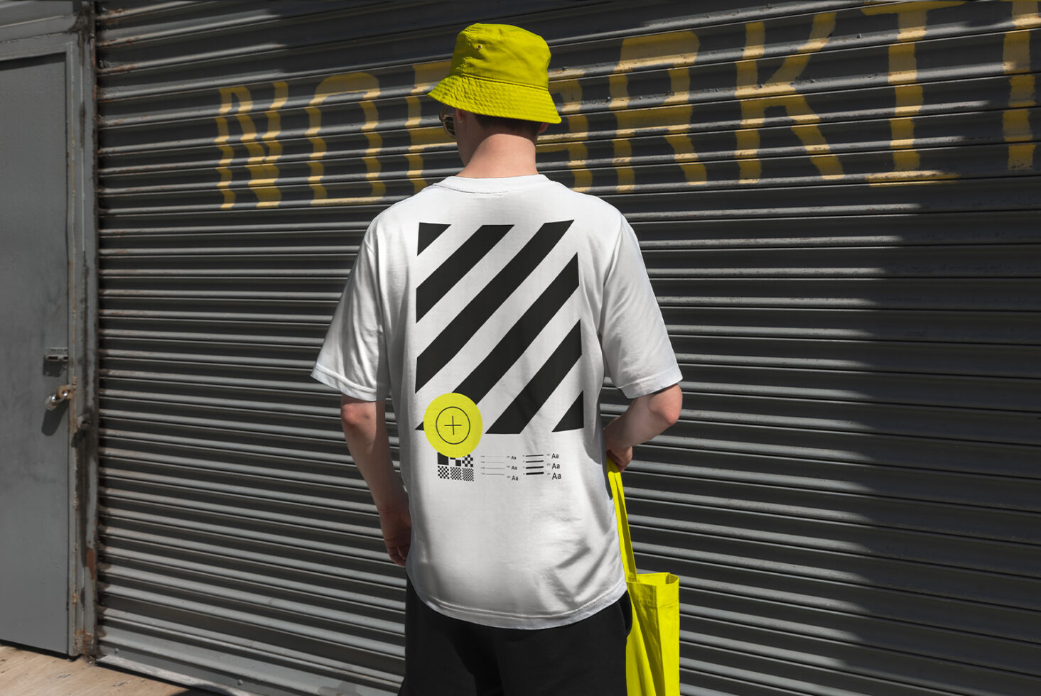 Person wearing a graphic T-shirt with bold black and white stripes design standing against a shutter background. Ideal for fashion mockup templates.