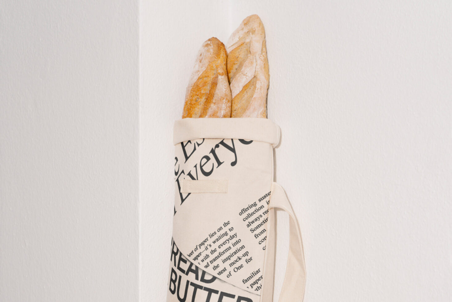 Canvas tote with bold typography design holding two baguettes against white wall. Perfect for product mockups or graphic design projects.