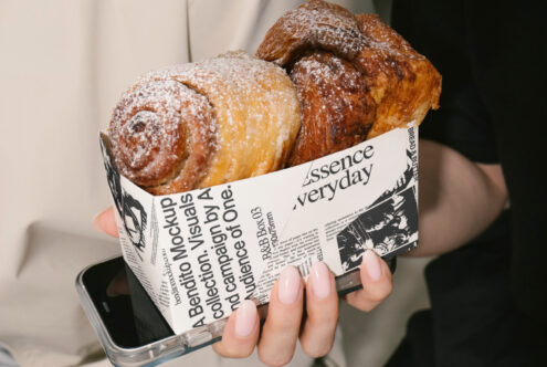 Mockup of a hand holding croissants in a paper box with typography design. Ideal for graphic designers and template creators seeking food packaging visuals.