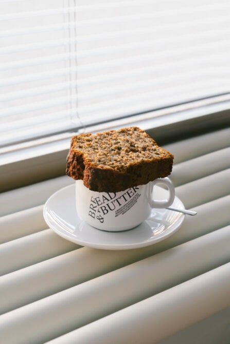Whole grain toast balancing on Bread & Butter branded mug on saucer near blinds