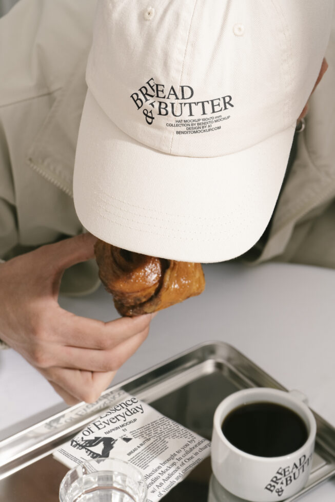 Designer cap mockup featuring bold typography Bread and Butter with a person eating a pastry next to a coffee cup on a tray SEO keywords: designer mockups.