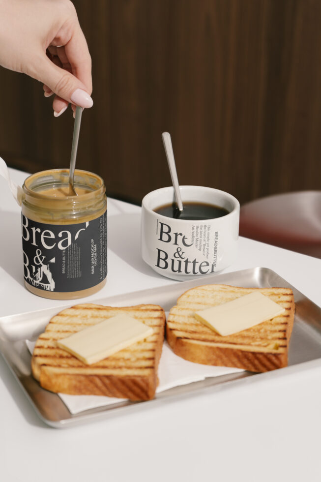 Breakfast scene with coffee mug and peanut butter jar mockups on a table; grilled bread with butter on a tray; ideal for design projects and templates.