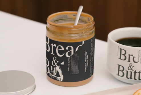 Peanut butter jar and coffee cup branding mockup on a table. Ideal for showcasing design templates and label graphics to creative professionals.