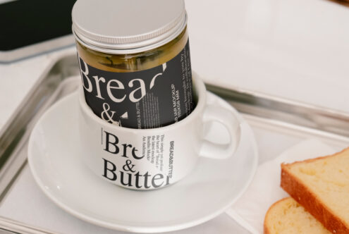 Mockup image showing a jar with Bread and Butter label placed in a coffee cup on a tray beside bread slices. Ideal for designers in packaging projects.