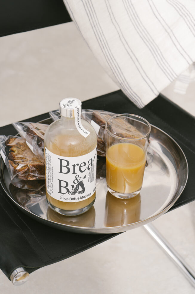 Juice bottle mockup with orange juice on a metal tray beside snack packs on a chair Elegant mockup design for branding SEO keywords Designers Marketplace