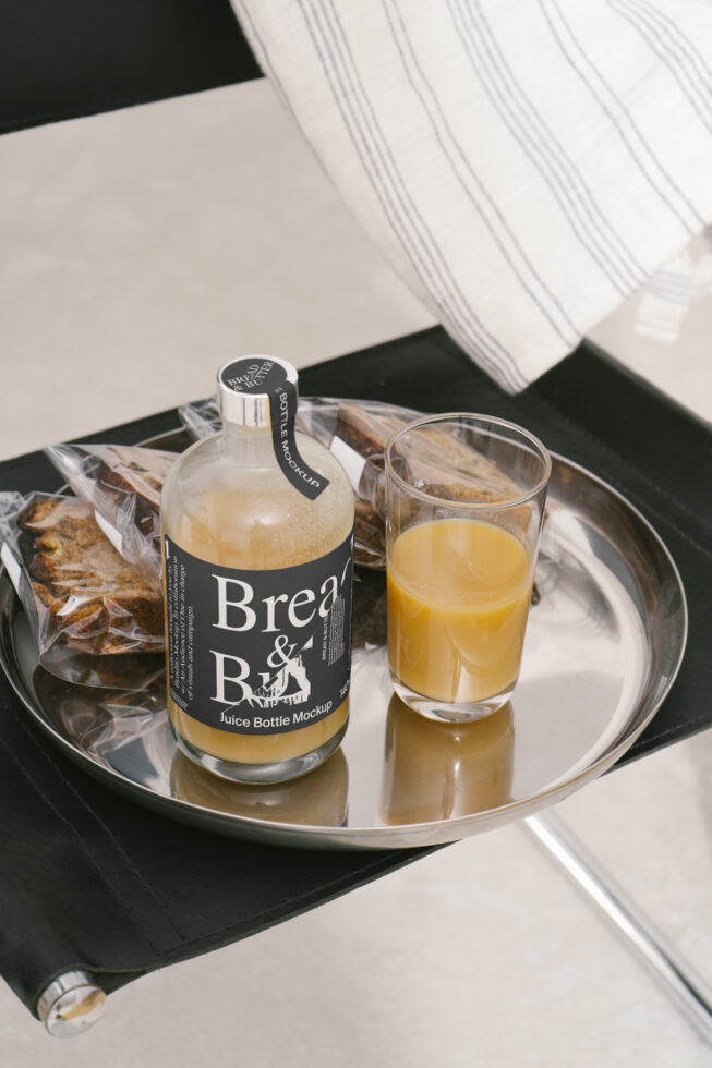 Juice bottle mockup on a silver tray with packaged bread slices and glass of orange juice. Ideal for designers seeking realistic kitchen product mockups.