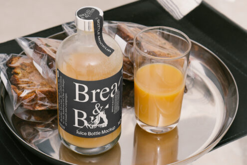 Juice bottle mockup on a tray with glass of orange juice and wrapped bread slices. Ideal for designers seeking food and beverage packaging templates.