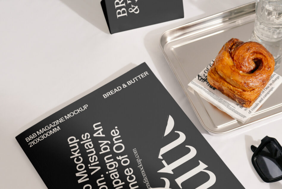 Dark magazine mockup with croissant on metal tray, sunglasses, water glass