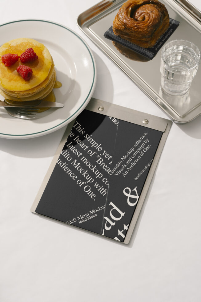 Top view of a breakfast scene with pancakes topped with berries, a pastry, and a mockup menu on a metal clipboard. Ideal for food and menu design.