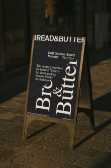 Dark outdoor sandwich board with wooden frame showing Bread & Butter branding in urban setting