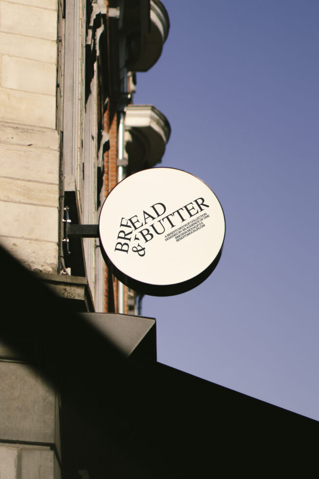 Round shop sign on old building facade reads Bread and Butter perfect for branding mockups urban design templates signage fonts blue sky.