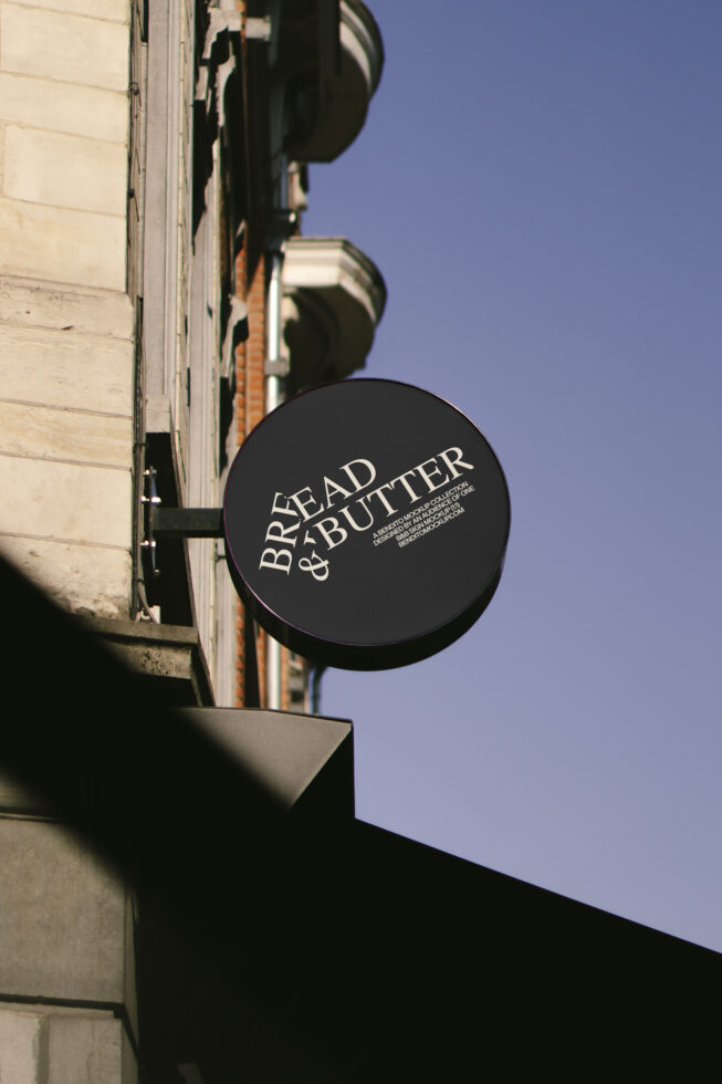 Round black store sign with Bread & Butter text on urban building background. Perfect for logo mockups, branding design, and signage template assets.