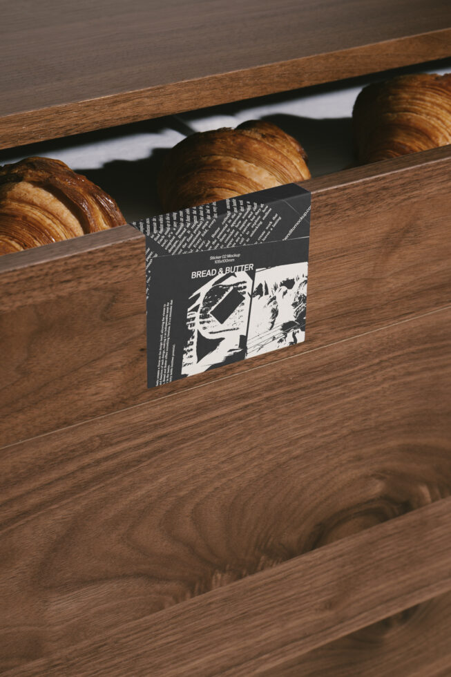 Wooden drawer mockup with croissants and a black and white sticker design. Perfect for designers seeking realistic branding and packaging visuals.