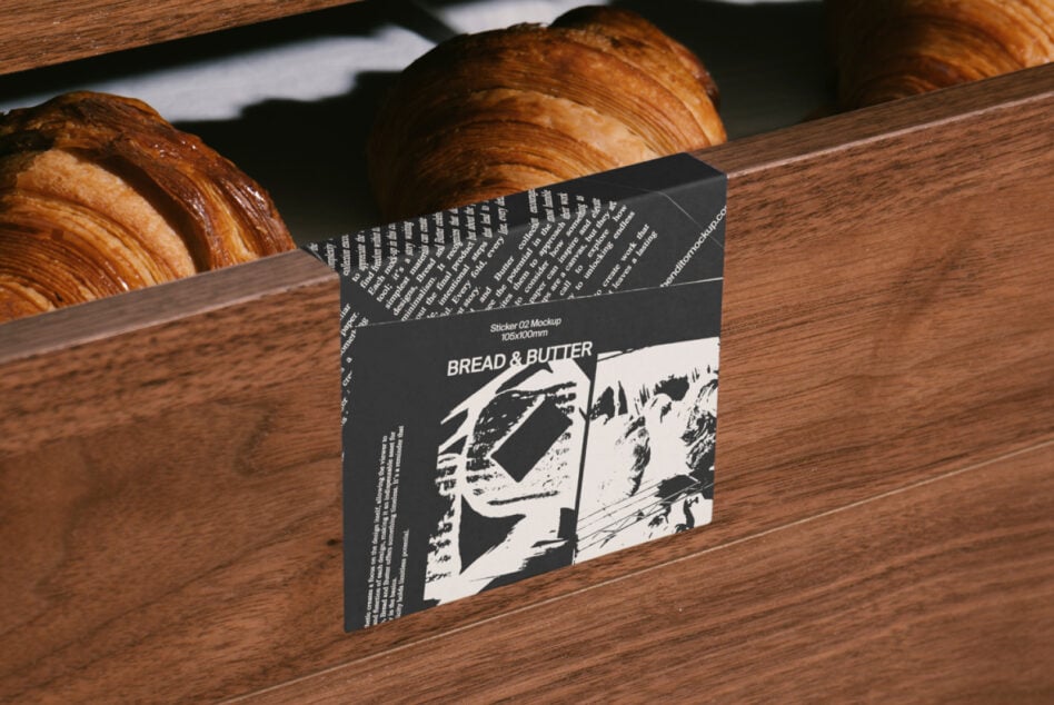 Dark sticker mockup on wooden surface with fresh croissants in background