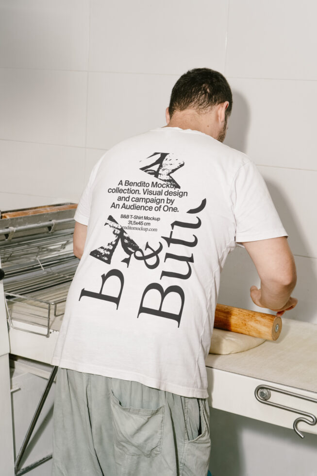 Man wearing a T-shirt with bold typography leaning over a table rolling dough. Perfect for mockup templates. Ideal for modern design projects.