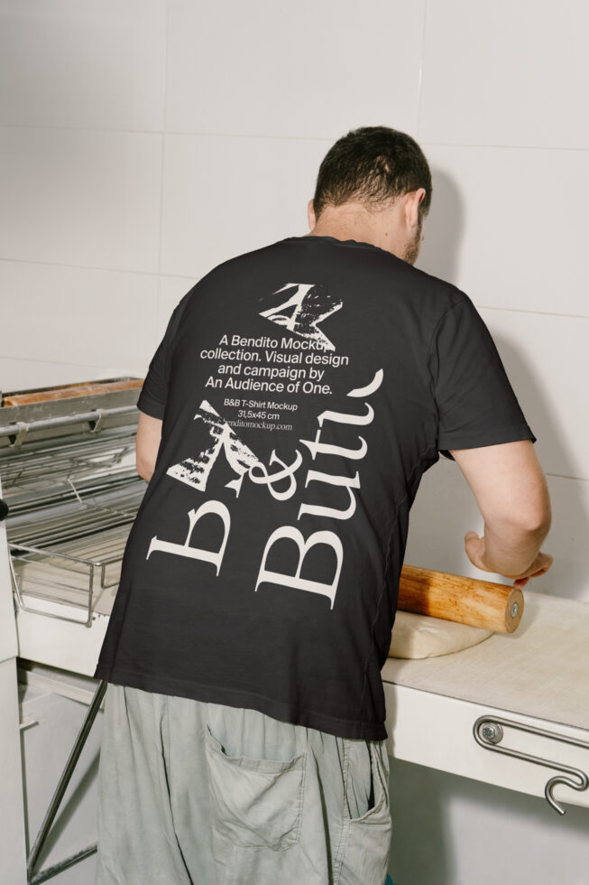 Man wearing a black T-shirt mockup with bold text, standing in a kitchen kneading dough. Ideal for clothing designers and mockup presentations.