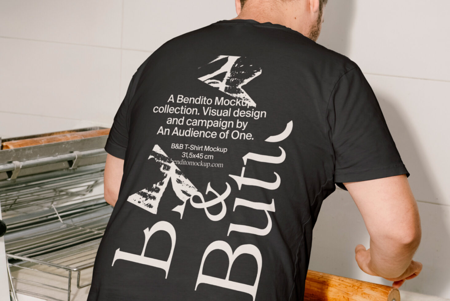 A man wears a black T-shirt with Bendito Mockup design text in white showcasing typography. Perfect for designers seeking stylish T-shirt graphics.