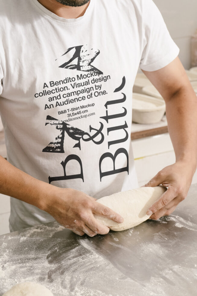 Person wearing a graphic t-shirt kneading dough on a floured surface; ideal for t-shirt mockup projects, graphic design, bakery themes in design.