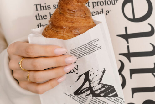 Hand holding croissant in paper bag with bold typography background. Ideal for branding mockups, editorial design, packaging concepts, font inspiration.