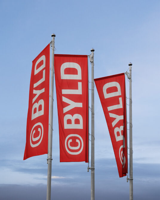 Three red banners on poles with white BYLD text on blue sky background