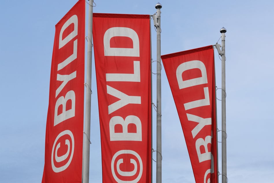 Red vertical banners with white BYLD lettering against cloudy sky