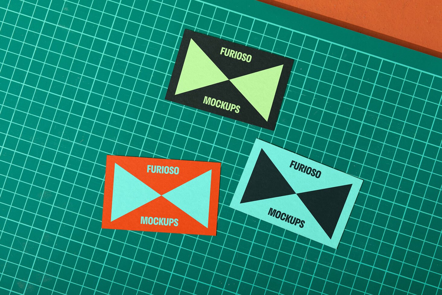 Three colorful business card mockups with modern geometric design on a grid cutting mat background. Perfect for designers showcasing branding visuals.
