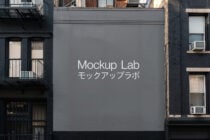 Gray building billboard mockup between urban brick structures with white Mockup Lab text