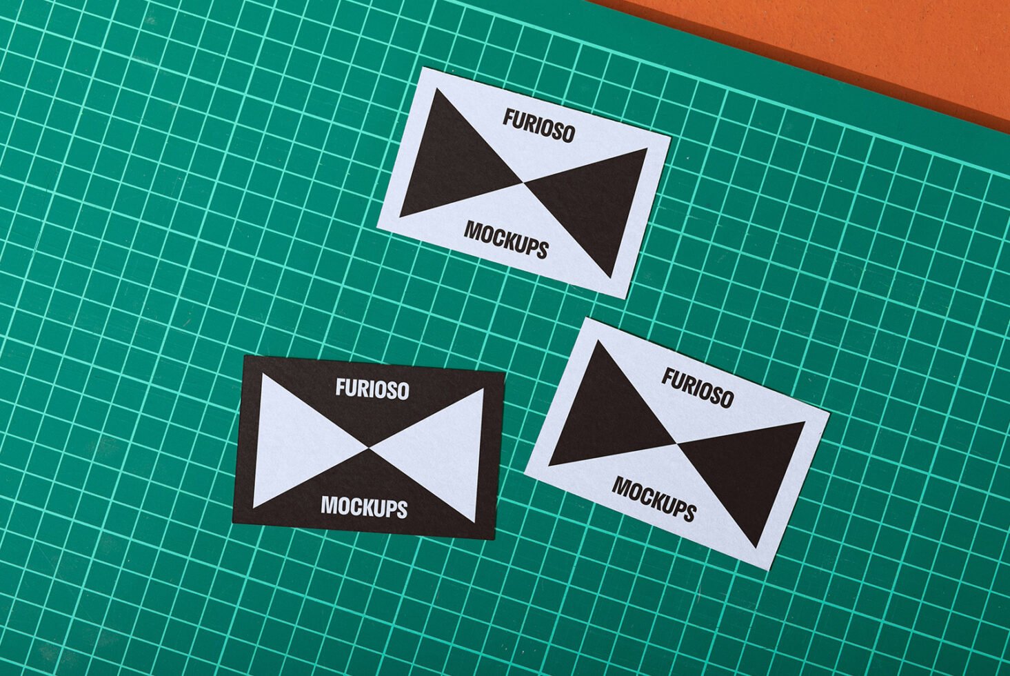 Card mockups with bold black and white geometric design on a green cutting mat. Ideal for graphic designers. Keywords: mockup, card, graphic design.