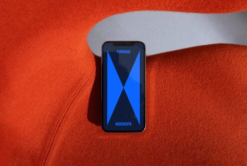 Smartphone mockup with blue geometric design on screen placed on vibrant orange fabric. Perfect for showcasing app designs. Ideal for designers.