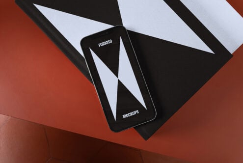 Smartphone mockup on geometric black and white book cover on red table ideal for designers showcasing modern branding and digital designs.
