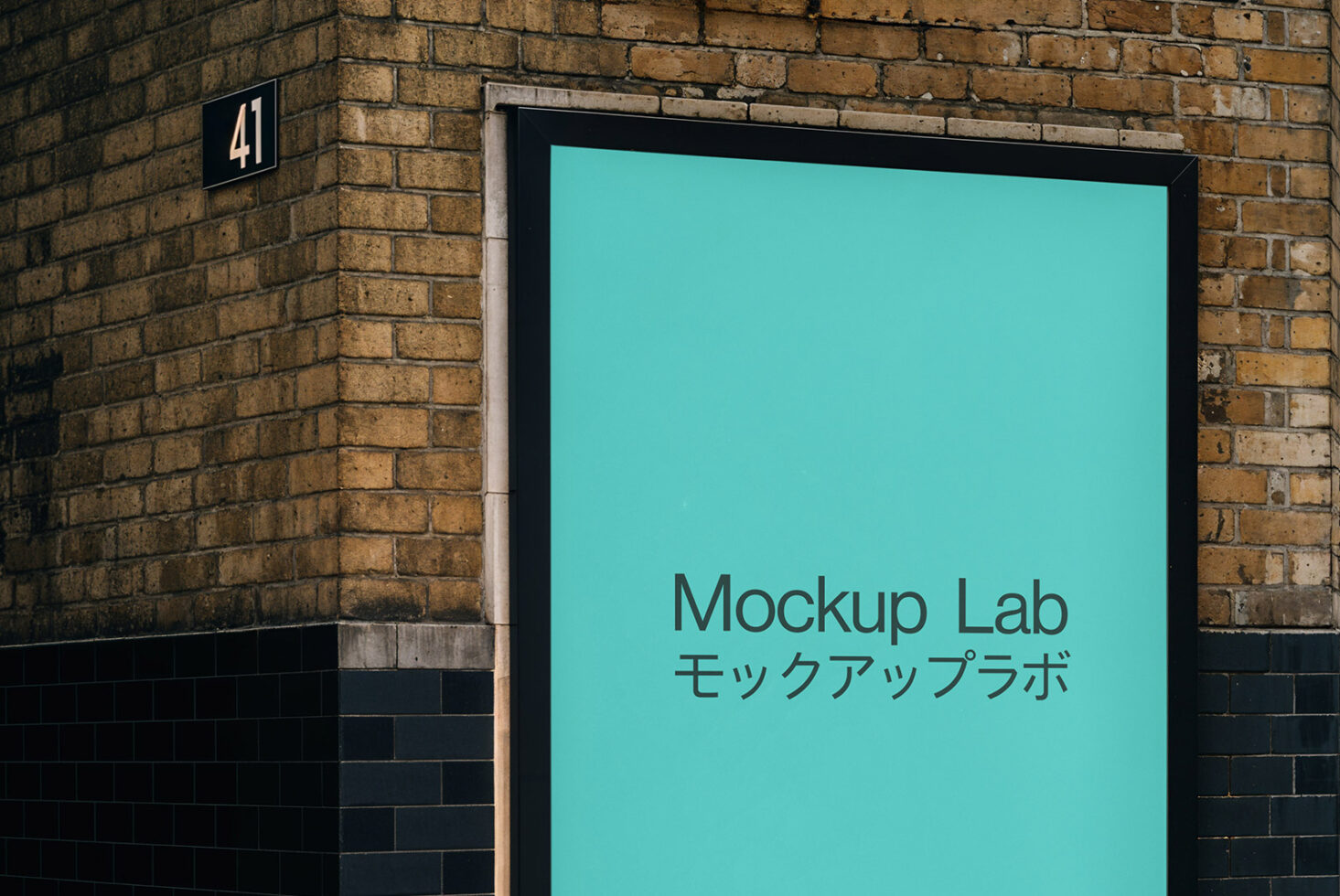 Street sign on brick wall displaying turquoise lightbox with Mockup Lab text in English plus Japanese characters
