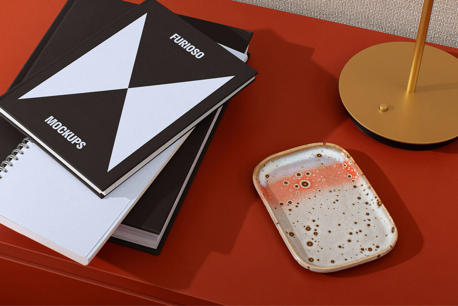Designer workspace with mockup notebooks on a red desk, ceramic tray, and modern gold lamp for creatives seeking stylish templates and unique assets.