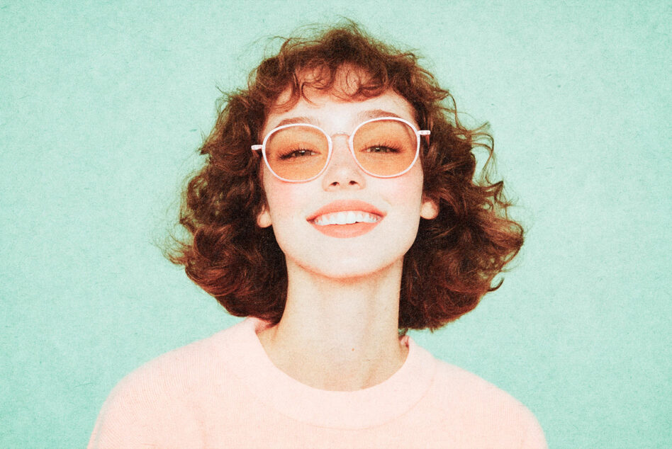 Person with short curly red hair wearing white round glasses smiling