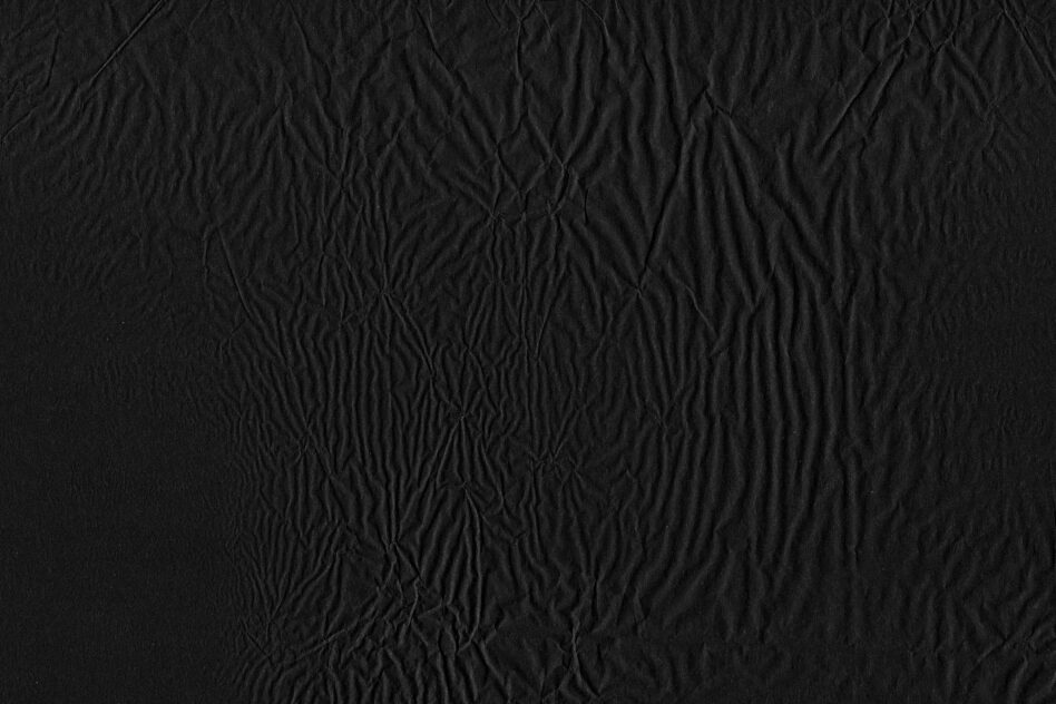 Close up of black crinkled fabric with deep wrinkles creating abstract shadow patterns