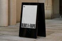 Double-sided A-frame sign with white text on black background in architectural courtyard