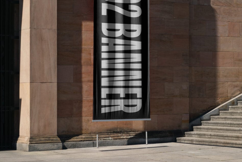 Vertical banner with metallic lettering hung on brick building facade casting shadows