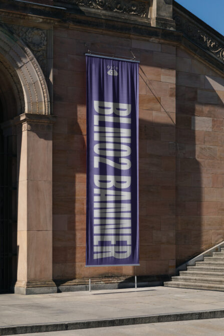 Purple fabric banner with white striped letters on historic stone architecture
