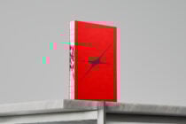 Red hardcover book with abstract design stands vertically on a marble surface photographed in a minimalist setting for designers mockup graphics template asset.