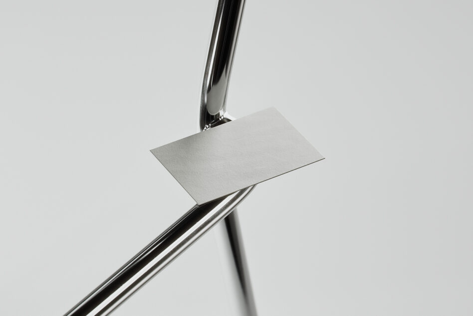 Blank business card held by chrome pen on crossed metal rods