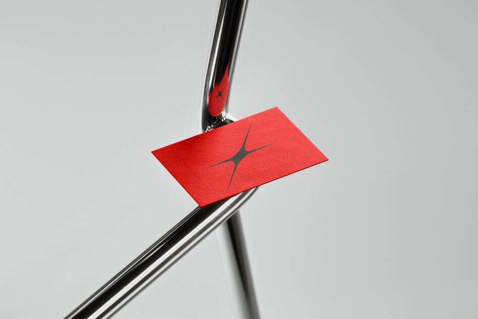 Red business card with geometric logo held by chrome pen on metal