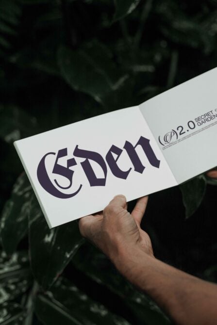 Open book displaying Gothic font with the word Eden held by hands. Nature background. Ideal for designers seeking typography graphics templates.