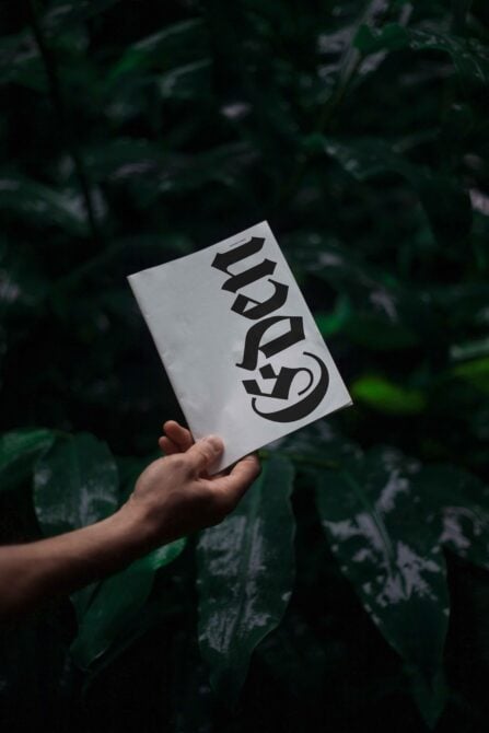 Hand holding a white mockup booklet with bold black typography design in a lush green natural background ideal for designers and creatives Mockups Graphics