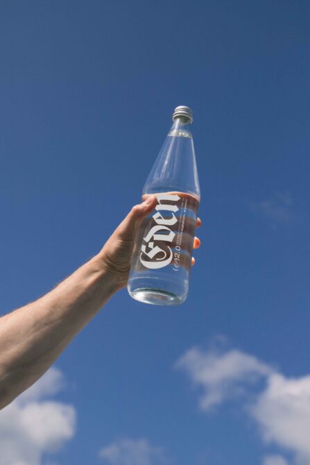 Clear glass bottle held up against bright blue sky with clouds