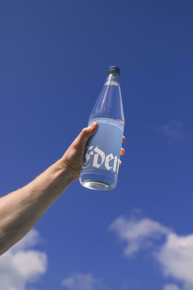 Hand holding a glass water bottle against clear blue sky; perfect for branding mockups; features elegant label design; ideal for creative projects.