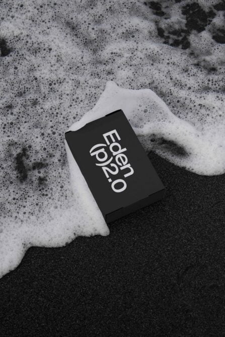 Black business card with white Eden logo in foam, sitting on dark sand beach